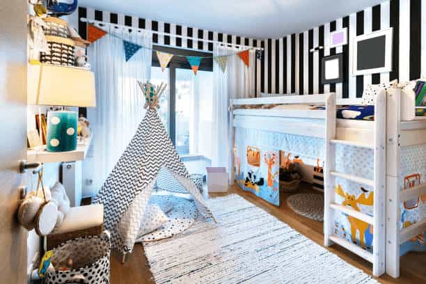 A kids' bedroom featuring a white bunk bed over a play area, a black and white striped accent wall, and a patterned teepee sitting on a textured rug.